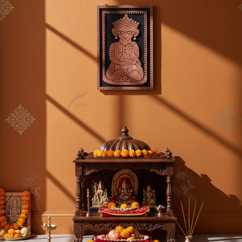 Lifestyle photography of the Janani Durga and Baby Ganesha terracotta wall relief displayed above a wooden home temple (Mandir). The scene features a textured ochre wall, marigold garlands, and burning incense, showcasing the artwork as a focal point for traditional Indian prayer room decor.