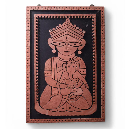 A handcrafted terracotta wall relief panel depicting the Hindu Goddess Durga in her 'Janani' (Mother) form, wearing a traditional crown and jewelry while cradling baby Ganesha on her lap. The reddish-brown clay figures are stylized in Indian folk art fashion and mounted on a contrasting black background, framed by a decorative perforated terracotta border.