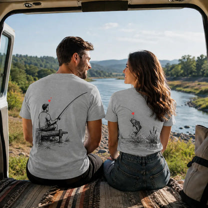 A man and a woman sit inside a vehicle facing a river landscape, wearing matching light gray graphic T-shirts with black fishing illustrations and a small red heart detail.