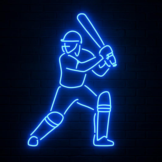A vibrant blue LED neon sign depicting a cricket player in a dynamic batting stance. The illuminated outline highlights the batsman's helmet, pads, and raised bat against a dark brick wall background. This modern sports wall art is designed for game rooms, man caves, and cricket enthusiasts' bedrooms.