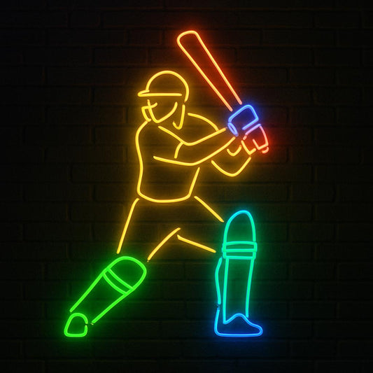 A vibrant LED neon sign featuring a cricket player in a dynamic batting stance ready to strike. The illuminated design outlines the batsman in yellow with a bright orange bat, accented by a green front pad and blue back pad against a dark brick wall background. Perfect wall art for sports bars, cricket clubs, or a fan's game room.