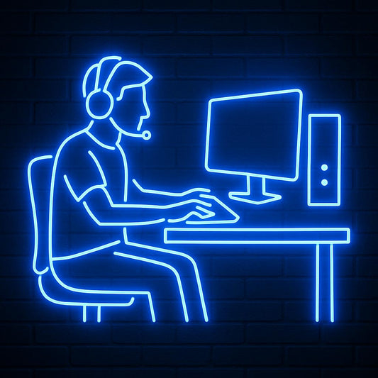 An electric blue LED neon sign depicting a gamer sitting at a computer desk wearing a headset with a microphone. The illuminated outline features a monitor, keyboard, and PC tower against a dark brick background, making it ideal decor for gaming rooms, esports lounges, or streaming studios.