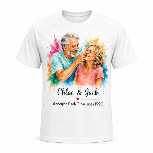 A white unisex t-shirt featuring a custom watercolor portrait of a smiling older couple surrounded by vibrant paint splatters, with funny anniversary text below. Free shipping by Incotta.
