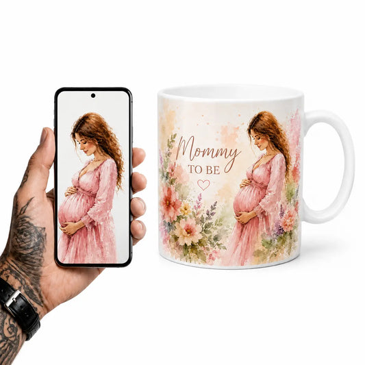 A beautifully customized glossy white ceramic coffee mug featuring a delicate watercolor portrait of an expecting mother in a pink dress, surrounded by pastel spring flowers and "Mommy TO BE" text. Lifestyle image.