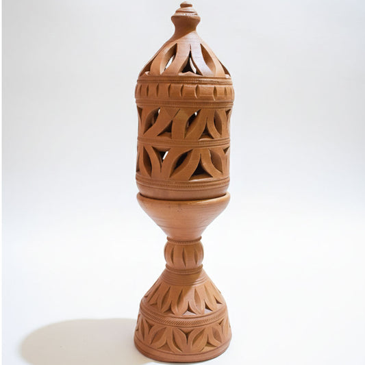 A vertical studio product shot of a decorative terracotta lamp isolated on a white background. The lamp features a removable conical lid, a pedestal base, and intricate geometric leaf-shaped cutouts throughout the body.