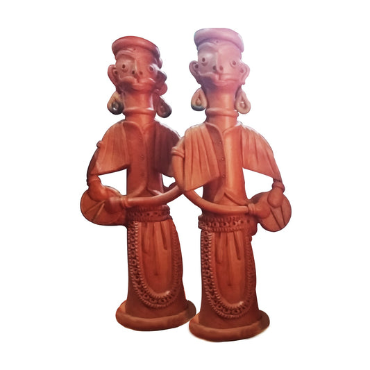 A front view of a pair of handcrafted terracotta figurines depicting traditional musicians playing drums (dhol). These standing clay dolls feature intricate detailing on their attire and jewelry, showcasing the rustic charm of Indian folk art with a natural reddish-brown finish against a white background.