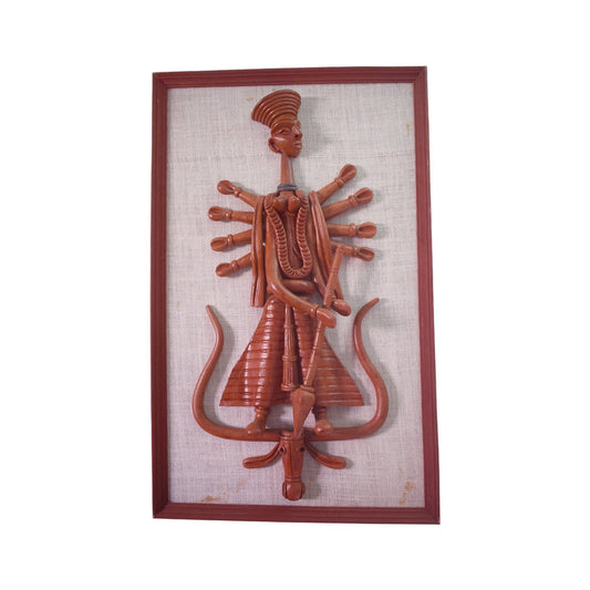 Front view of a framed terracotta wall hanging depicting the Goddess Durga in a stylized, multi-armed form, standing atop a vehicle figure. The reddish-brown clay sculpture is mounted on a textured fabric backing, representing traditional Panchmura folk art craftsmanship.