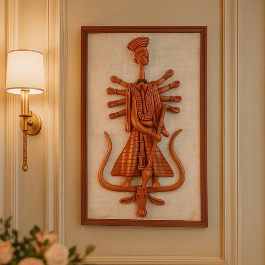 Front view of a framed wall hanging featuring a stylized terracotta sculpture of Goddess Durga with multiple arms, crafted in the traditional Panchmura style. The reddish-brown clay figure is mounted on a textured beige fabric backing within a wooden frame.