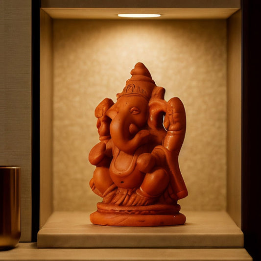 A close-up side view of a handcrafted terracotta Lord Ganesha statue displayed within an illuminated wall niche. The warm downlighting highlights the intricate clay details and side profile of the eco-friendly idol, creating a serene spiritual focal point.
