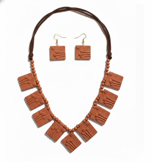 A top-down view of a traditional terracotta jewelry set isolated on a white background. The set features a statement necklace composed of multiple fish-shaped clay pendants with textured detailing, strung together with small round earthen beads. Beside the necklace is a matching pair of fish-motif drop earrings on gold-tone hooks, showcasing a natural reddish-brown clay finish.