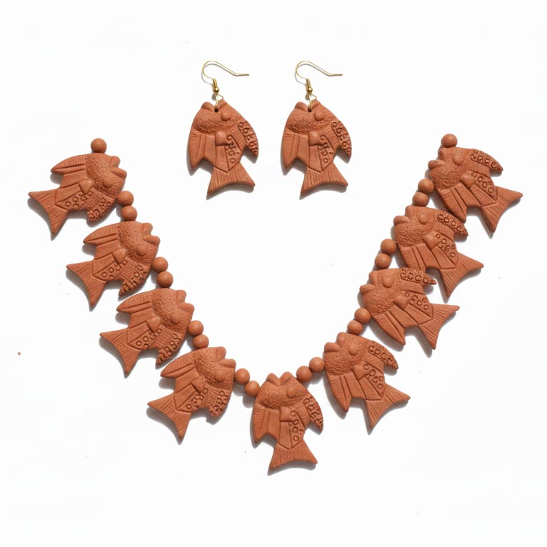 A top-down view of a traditional terracotta jewelry set isolated on a white background. The set features a statement necklace composed of multiple fish-shaped clay pendants with textured detailing, strung together with small round earthen beads. Beside the necklace is a matching pair of fish-motif drop earrings on gold-tone hooks, showcasing a natural reddish-brown clay finish.